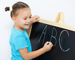 Image showing Little girl is writing on a blackboard