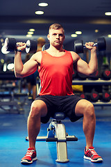 Image showing young man with dumbbells flexing muscles in gym