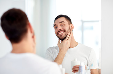 Image showing happy man applying aftershave at bathroom mirror