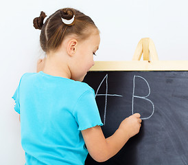 Image showing Little girl is writing on a blackboard