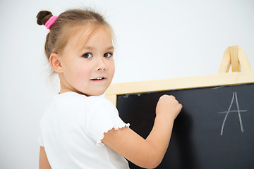 Image showing Little girl is writing on a blackboard