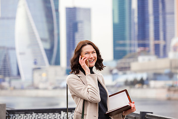 Image showing smiling middle-aged woman with notebook talking on the phone