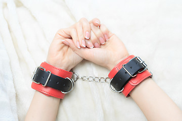 Image showing female hands in leather handcuffs. on the background sheet. sex toys.