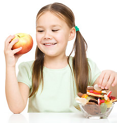 Image showing Little girl choosing between apples and sweets