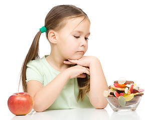 Image showing Little girl choosing between apples and sweets