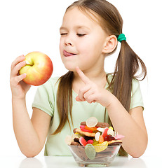 Image showing Little girl choosing between apples and sweets