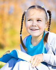 Image showing Little girl is reading a book outdoors