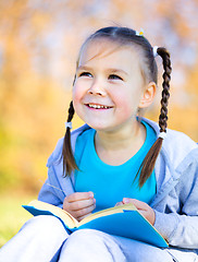 Image showing Little girl is reading a book outdoors