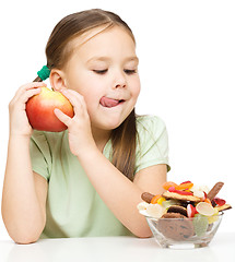 Image showing Little girl choosing between apples and sweets