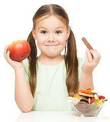 Image showing Little girl choosing between apples and sweets