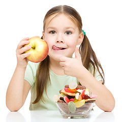 Image showing Little girl choosing between apples and sweets