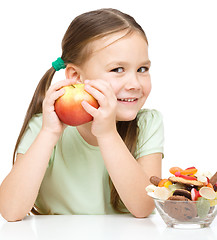 Image showing Little girl choosing between apples and sweets