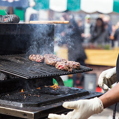 Image showing Beef burgers being grilled on food stall grill.