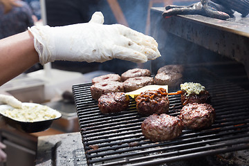 Image showing Beef burgers being grilled on food stall grill.