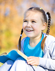 Image showing Little girl is reading a book outdoors