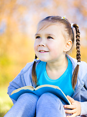 Image showing Little girl is reading a book outdoors