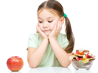 Image showing Little girl choosing between apples and sweets