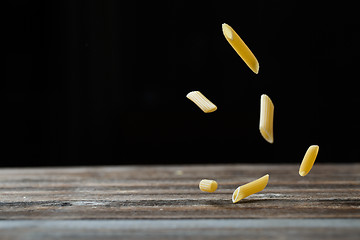 Image showing Falling penne pasta. Flying yellow raw macaroni over black background.