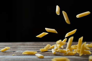 Image showing Falling penne pasta. Flying yellow raw macaroni over black background.