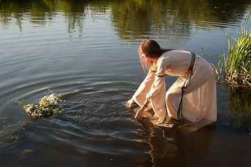 Image showing Attractive girl lowers wreath in water