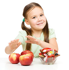 Image showing Little girl choosing between apples and sweets