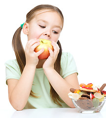 Image showing Little girl choosing between apples and sweets