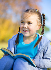 Image showing Little girl is reading a book outdoors