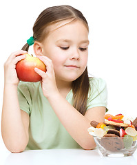 Image showing Little girl choosing between apples and sweets