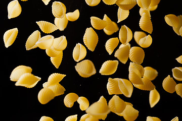 Image showing Falling conchiglie pasta. Flying yellow raw macaroni over black background.