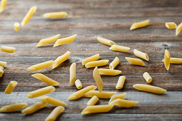 Image showing Falling penne pasta. Flying yellow raw macaroni over black background.