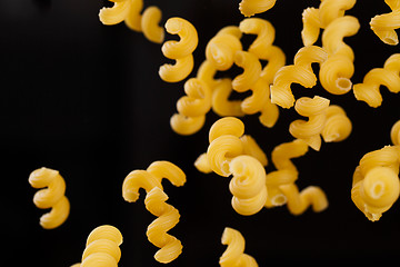 Image showing Falling cavatappi pasta. Flying yellow raw macaroni over black background. 