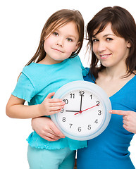 Image showing Little girl and her mother are holding a big clock