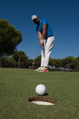 Image showing golf player hitting shot, ball on edge of hole