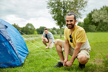 Image showing smiling friends setting up tent outdoors