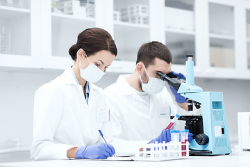 Image showing scientists with clipboard and microscope in lab