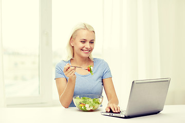 Image showing smiling woman with laptop eating salad at home