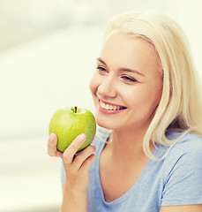 Image showing happy woman eating green apple at home