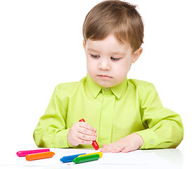 Image showing Little boy is drawing on white paper using crayon