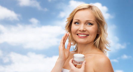 Image showing happy woman applying cream to her face