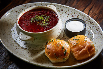 Image showing red borscht with sour cream, wild garlic, bread on a wooden background