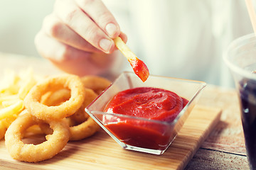 Image showing close up of hand dipping french fries into ketchup