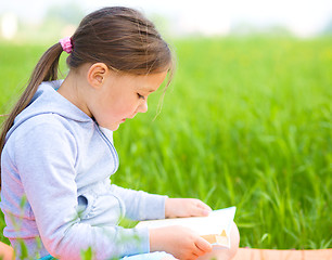 Image showing Little girl is reading a book outdoors