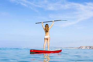 Image showing A beautiful and happy woman with arms up and learning paddle-sur