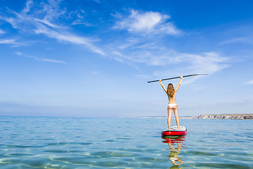 Image showing A beautiful and happy woman with arms up and learning paddle-sur