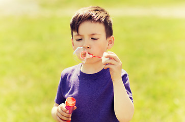 Image showing little boy blowing soap bubbles outdoors