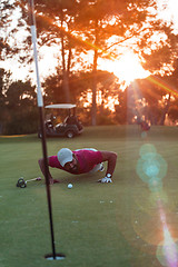 Image showing golf player blowing ball in hole with sunset in background