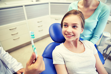 Image showing happy dentist showing toothbrush to patient girl