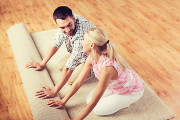 Image showing happy couple unrolling carpet or rug at home