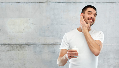 Image showing happy young man applying cream or lotion to face