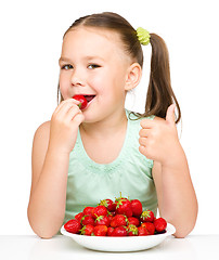 Image showing Happy little girl is eating strawberries